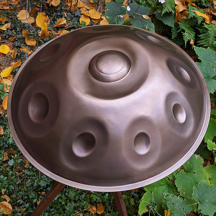 AYA Sounds Handpan aus Embersteel steht draußen zwischen Pflanzen und Bäumen auf einem Handpan Ständer