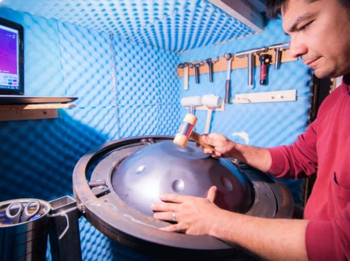 Handpan Maker arbeitet an einer Handpan. Im Hintergrund sieht man seine Werkzeuge an einer blauen Wand hängen.