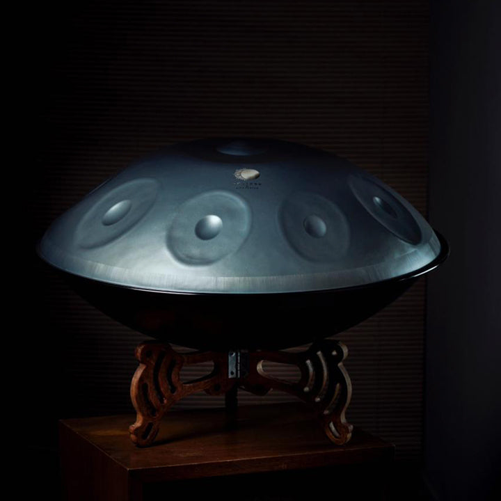 Eine nitrierte Eclipse Handpan Drum steht hell erschienen vor dunklem Hintergrund auf einen Katanui Handpan Ständer. Dieses günstige Handpan Instrument eignet sich gut für Anfänger und Einsteiger zum kaufen.