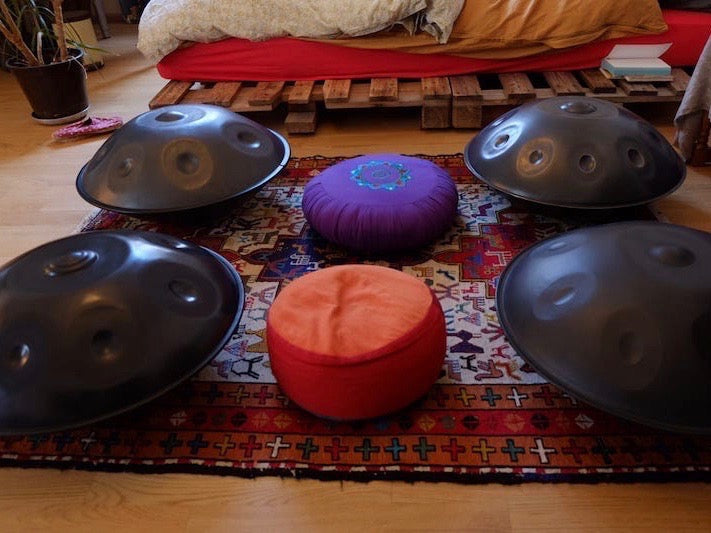 Vier Handpans liegen um zwei Meditationskissen auf einem roten Perserteppich auf dem Boden