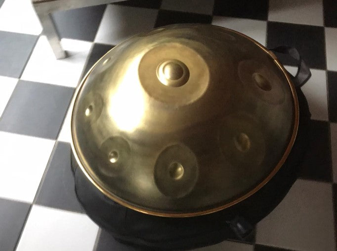 Eine goldene Handpan liegt in einem Handpan Case auf einem schwarz weiß karriertem Boden im Showroom Passau