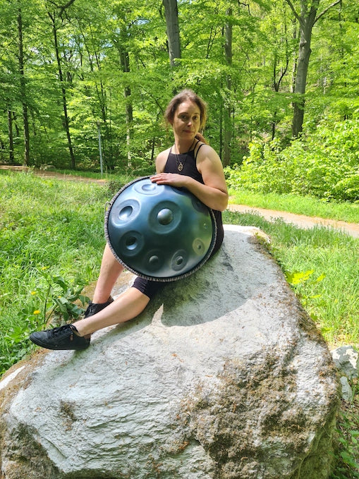 Die Handpan.World Vertreterin Sabrina aus dem Harz sitzt im Grünen auf einem Stein und hält eine Handpan im Arm. Handpan spielen lernen kannst Du im Harz.