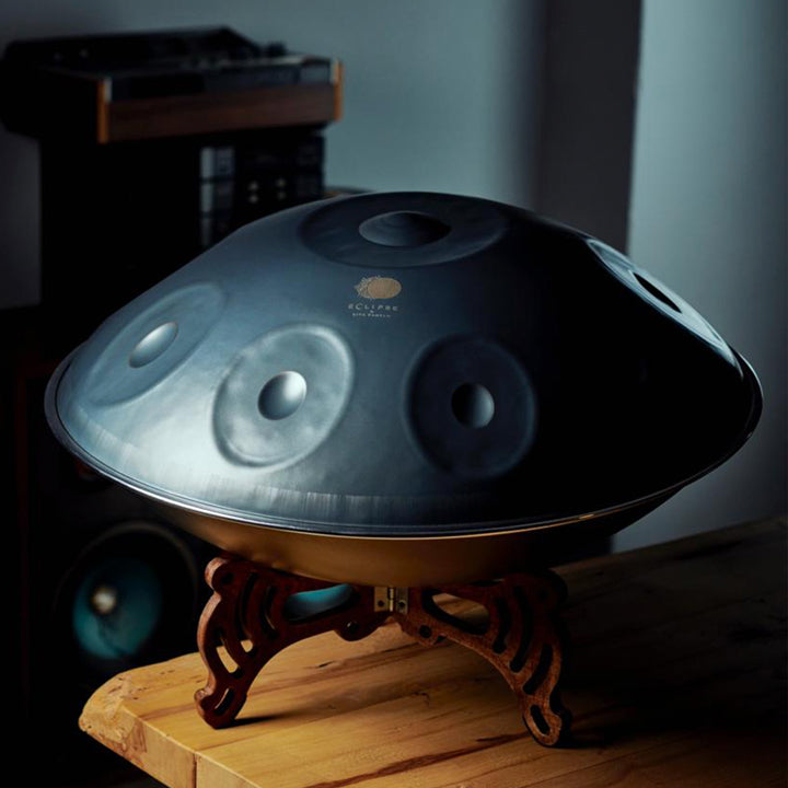 Eine schwarze Anfänger Handpan der Marke Eclipse steht auf einem Handpan Drum Ständer aus Holz in einem Handpan Geschäft. Dieses günstige Musikinstrument kann im Handpan.World Online Shop gekauft werden. 