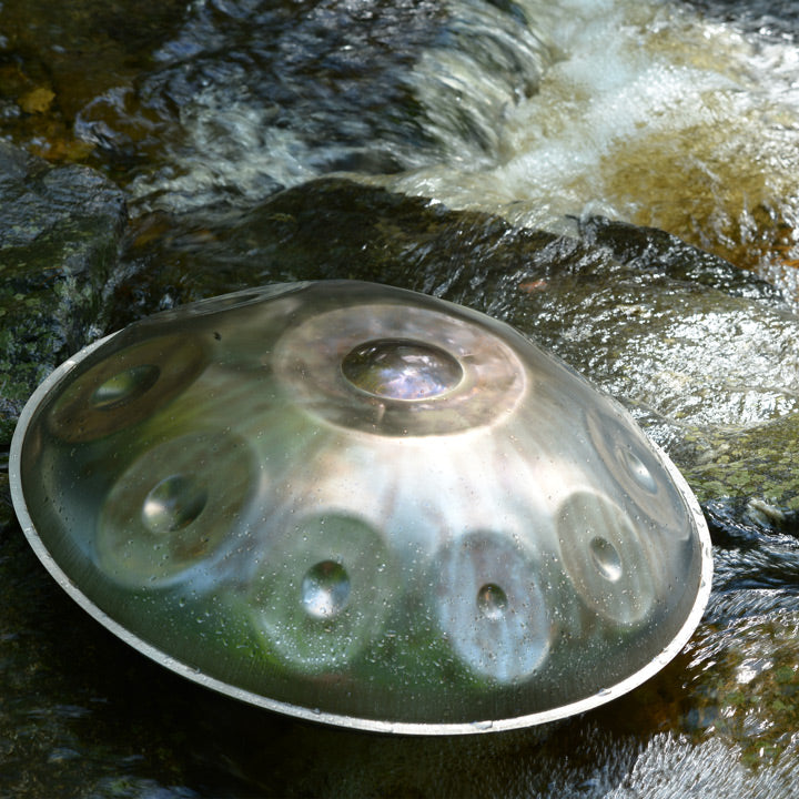 Eine Magical nitrierte Handpan liegt auf einem moosbedeckten Felsen neben einem ruhigen Bach in einer natürlichen Umgebung.