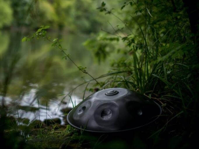 Nitrierte, silberschimmernde Handpan steht auf vermoosten Steinen. Im Hintergrund ist ein See zu sehen, welcher mit grünen Pflanzen umrandet ist.