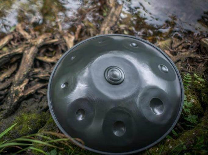 Nitrierte Handpan liegt auf großen Wurzeln eines Baumen. Dahinter liegen viele Äste und Zweige, die leicht im See verschwinden.