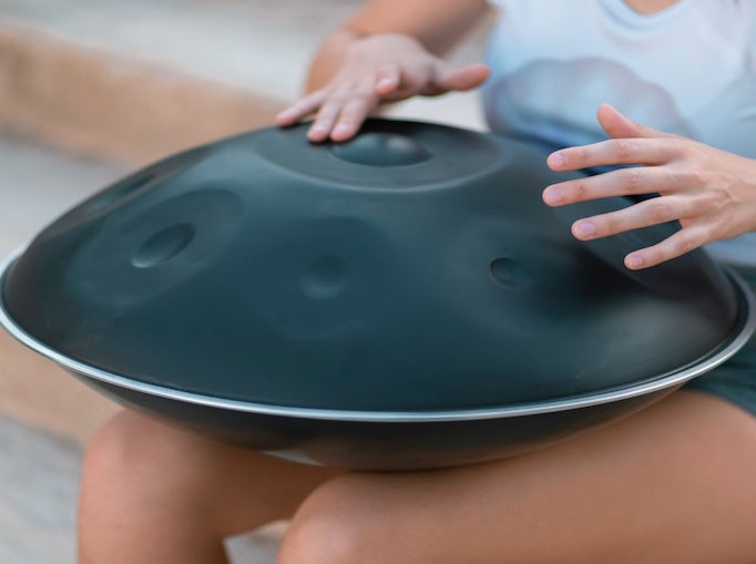 Eine Handpanspielerin sitzt auf Stufen und spielt eine schwarze nitrierte Handpan.