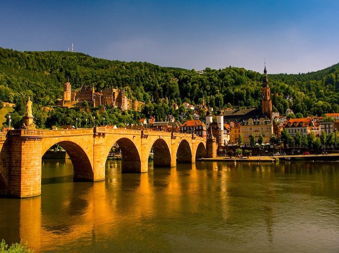 Die Alte Brücke in Heidelberg erleuchtet durch das Sonnenlich angestrahlt gelb golden und spielgelt sich im darunter fließenem Neckar.