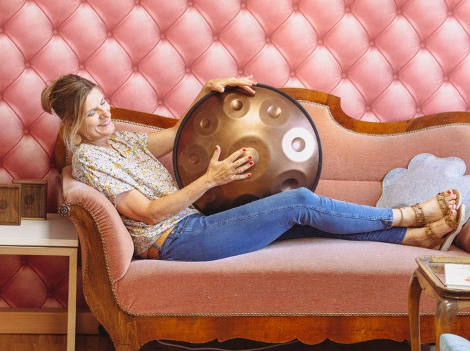 Die Handpan.world Vertreterin Anja Schmidt liegt mit einer Handpan auf einem rosafarbenen Sofa