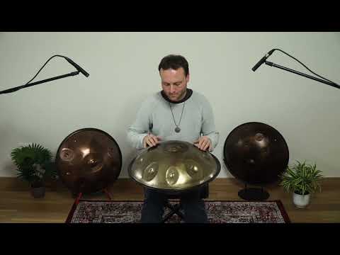 Mann sitzt in schön dekoriertem Zimmer von einer Silber golden schimmernden Edelstahl Handpan namens Spirit Sould B2 Celtic Minor / Amara 9 Edelstahl 440Hz. Im Hintergrund sind zwei weitere Handpans und Pflanzen zu sehen.