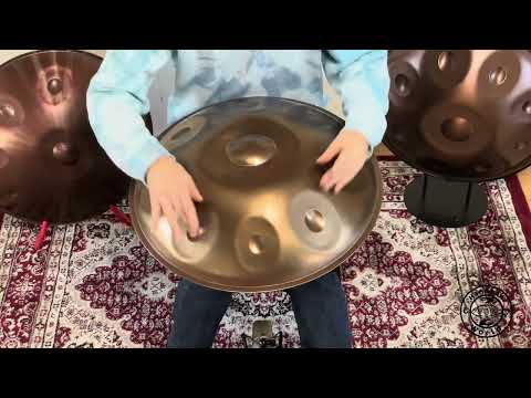 Ein Handpan-Spieler sitzt auf einem kunstvoll gestalteten Teppich, umgeben von Handpans, während er den schönen Klang des Magical A2 Celtic/Amara Handpans demonstriert.