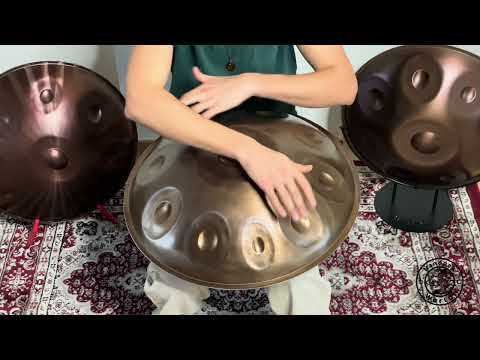 Ein Mann spielt eine wunderschöne NamiPan Handpan D Sabye mit 10 Noten, während er zwischen zwei glänzenden Handpans auf einem kunstvoll gemusterten Teppich sitzt.