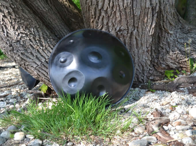 Nitrierte Handpan von Eternal Echoes lehnt an einem Baum hinter einem Büschel Gras. 