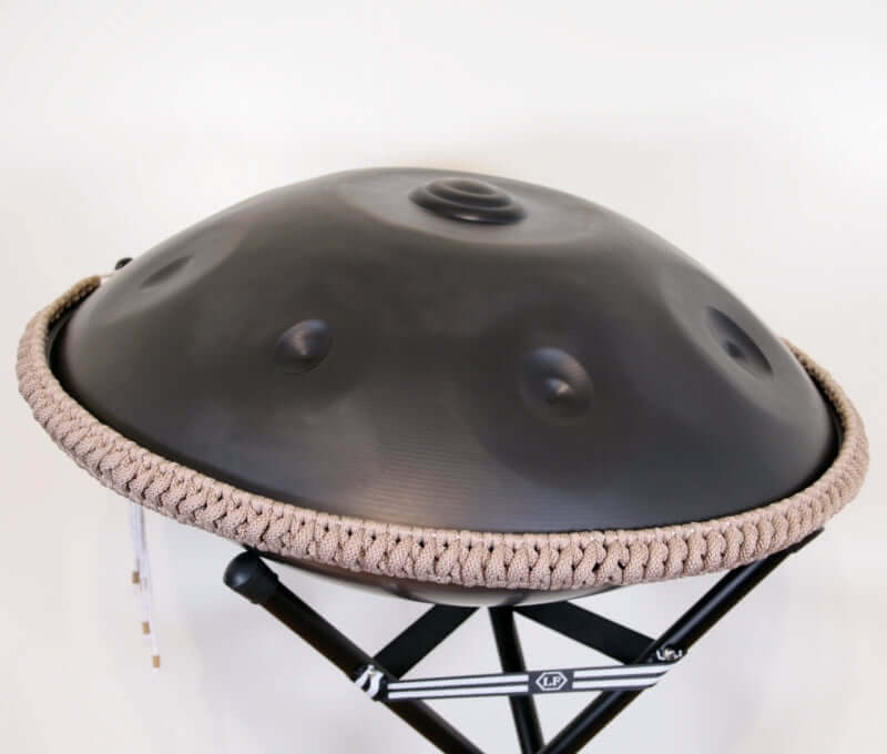 nitrierte, schwarze Handpan mit Handpan Rope auf einem Holzständer. Das Rope ist in der Farbe Beige.