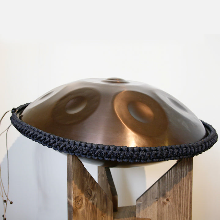 nitrierte, schwarze Handpan mit Handpan Rope auf einem Holzständer. Das Rope ist in der Farbe Dunkelgrau.