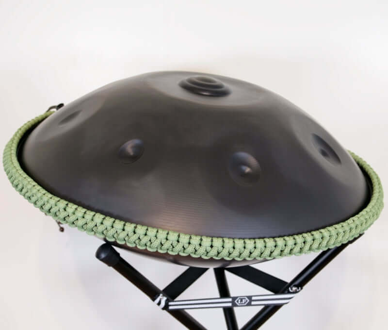 nitrierte, schwarze Handpan mit Handpan Rope auf einem Holzständer. Das Rope ist in der Farbe Hellgrün.