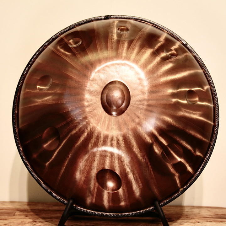 AeloPan Handpan Bronze glänzend steht auf einem Ständer vor weißer Wand. Man sieht die Handpan von vorne