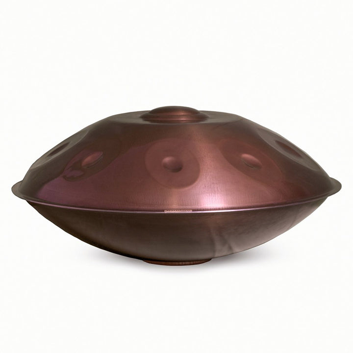 Eine Healing Frequency Handpan F2 Low Pygmy in einem bronzefarbenen Edelstahl mit rötlichen Schimmer und 9 sichtbaren Tonfeldern auf weißen Hintergrund.