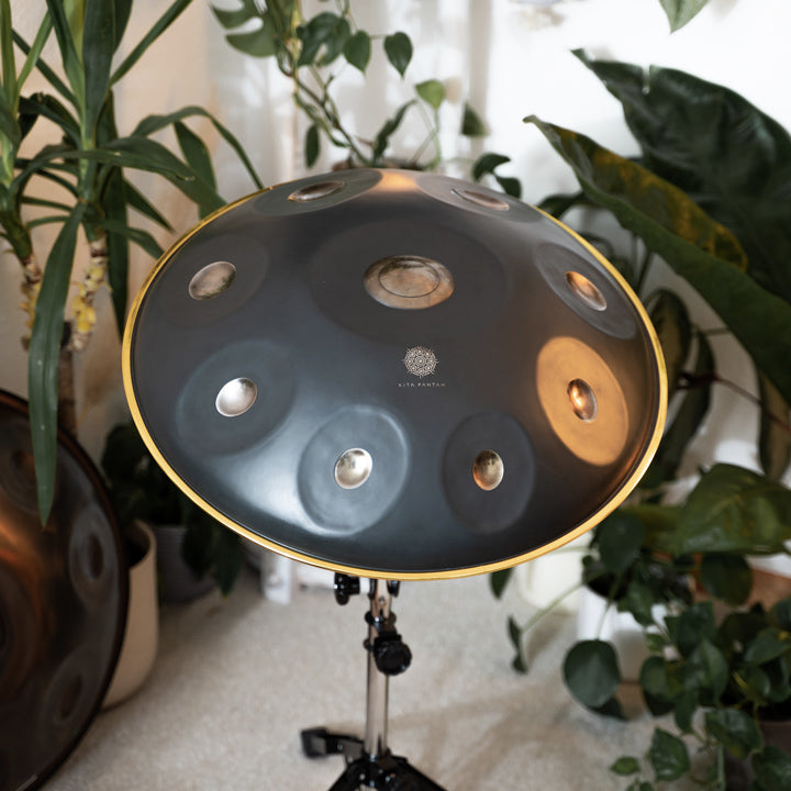 Kita Pantam in dem Design Polished Gold steht in einem gemütlichen Raum mit Pflanzen und anderen Handpans auf einem Handpan Ständer