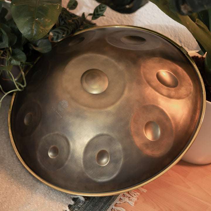 Handgefertigte KitaPantam Handpan in dem Design Gold Vintage liegt zwischen anderen Handpans und Pflanzen auf dem Boden