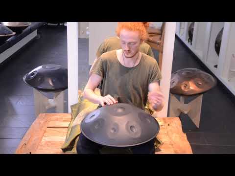 Rothaariger Handpanspieler mit grünem T-Shirt sitzt vor einem Spiegel und spielt eine Black Magic B2 Celtic Minor 9 Nitriert im Handpan.World Showroom.