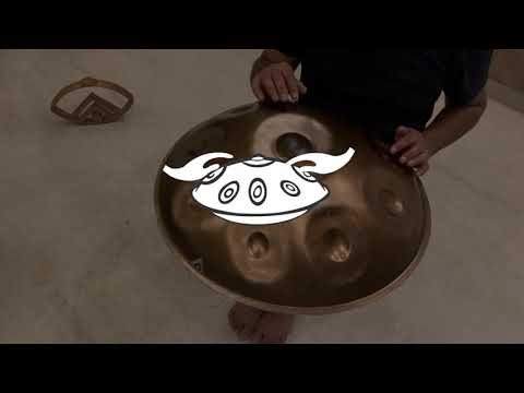 Ein Handpanspieler spielt eine Svaraa D Sabye. Man sieht einen Steinboden und das Svaraa Logo aus Holz im Hintergrund aufgestellt. Diese Handpan, sowie viele weitere kann man online im Handpan.World Store kaufen.