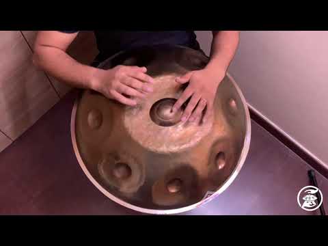 Hier sieht man einen Handpanspieler, der eine Svaraa F#2 Low Pygmy Edelstahl Handpan spielen. Die Handpan schimmert gülden und hat viele kleine Dellen vom aufwendigen Stimmprozess. Diese Handpan, sowie viele weitere kann man online im Handpan.World Store kaufen.