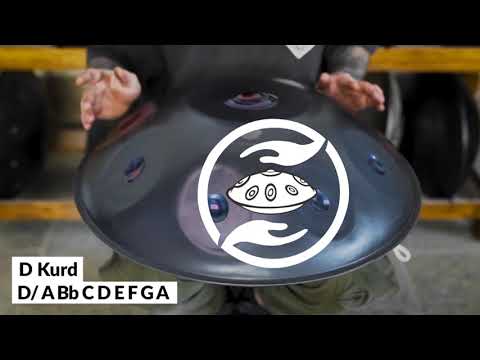 Ein Handpanspieler mit tattooierten Armen spielt eine nitrierte Kita D Kurd 9 violett poliert. Das Logo on Kita Pantam ist auf der handpan eingraviert. Im Hintergrund sieht man viele Handpans in einem Regal stehen.